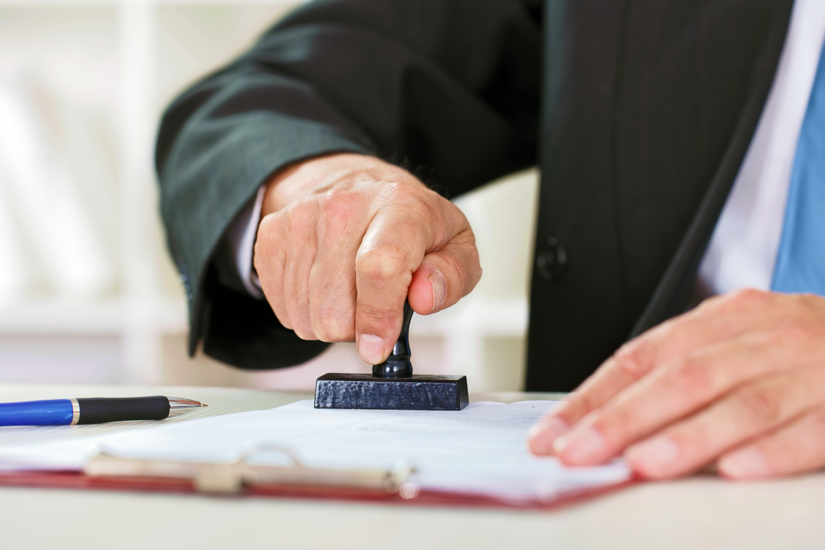 Image of a person in a suit physically stamping a piece of paper.