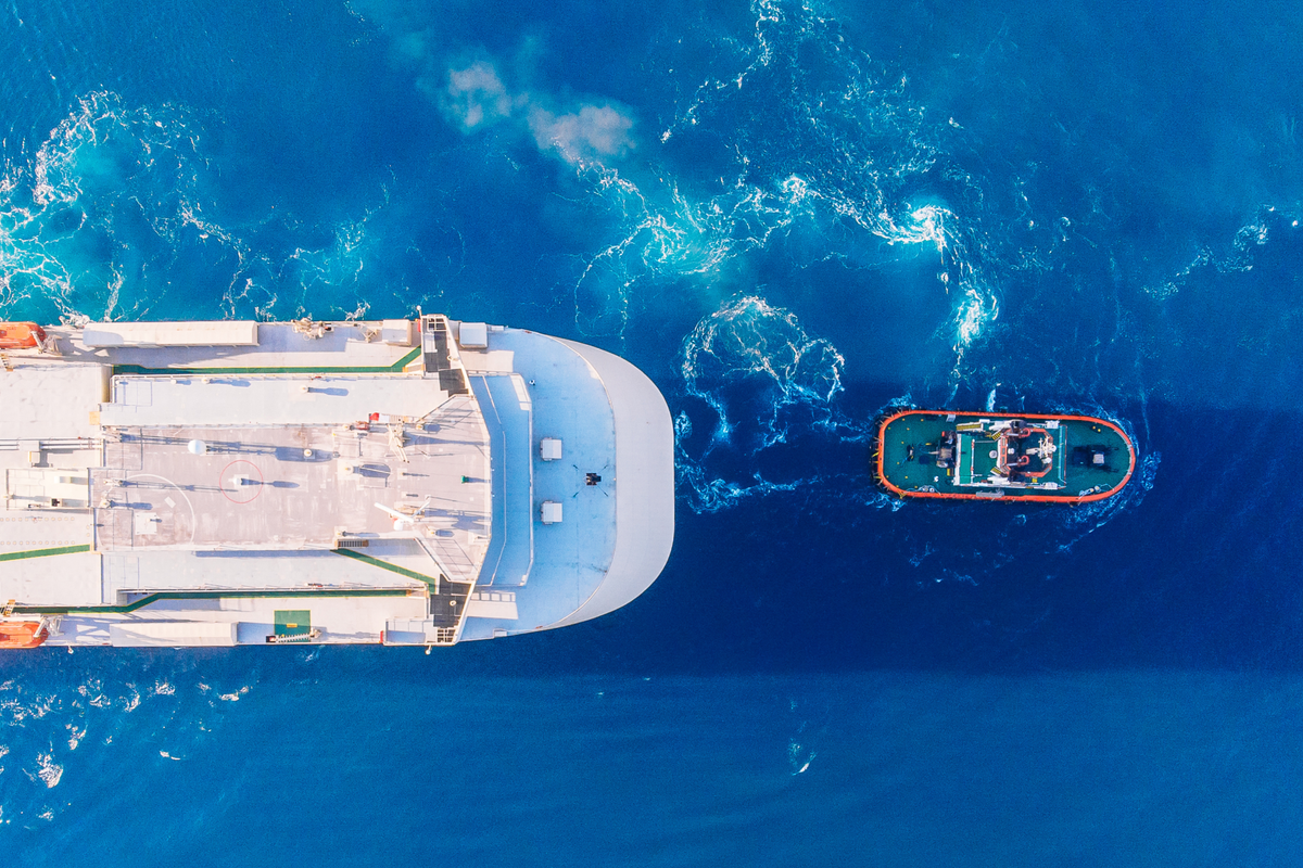 Image of a large ship being pulled by a tugboat, as seen from above.