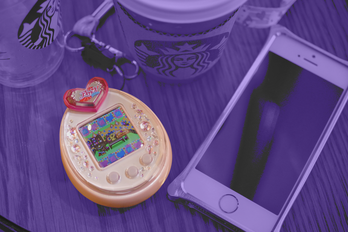 Image of a Tamagotchi next to a mobile phone, treated with a purple filter.