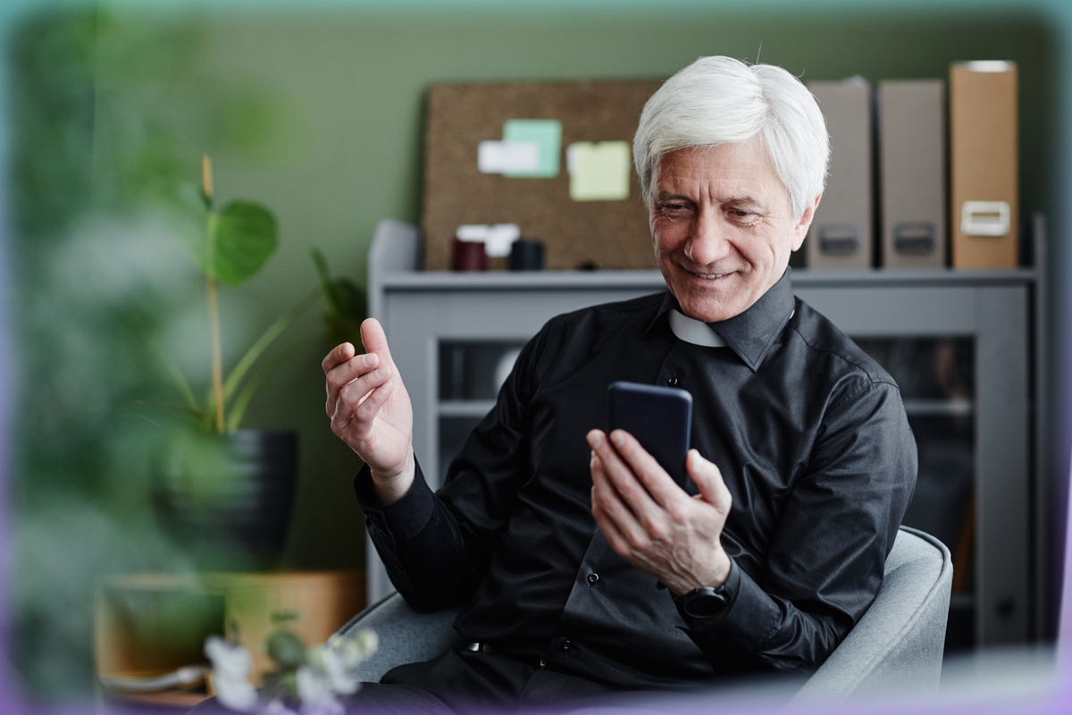 Photograph of a white-haired priest looking at the phone in his hand.