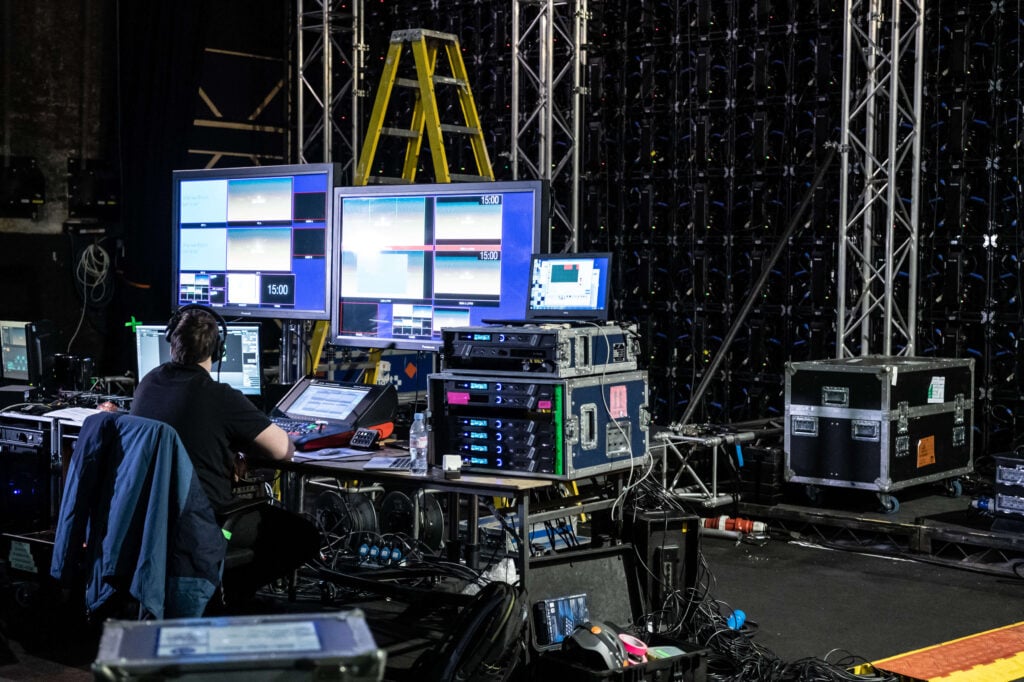 Image of a person sitting backstage in front of a lot of elaborate mixing equipment.