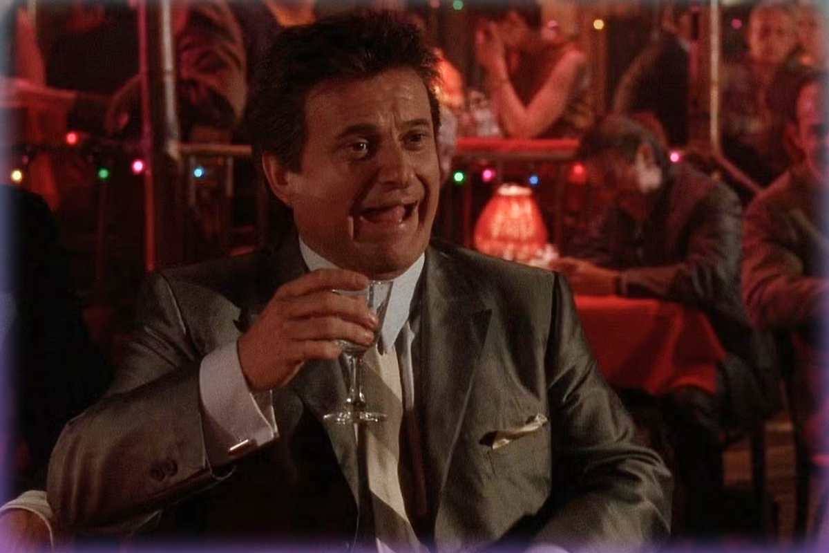Film still of Joe Pesci in an iconic scene from Goodfellas, sitting in a nightclub holding a cocktail and laughing.