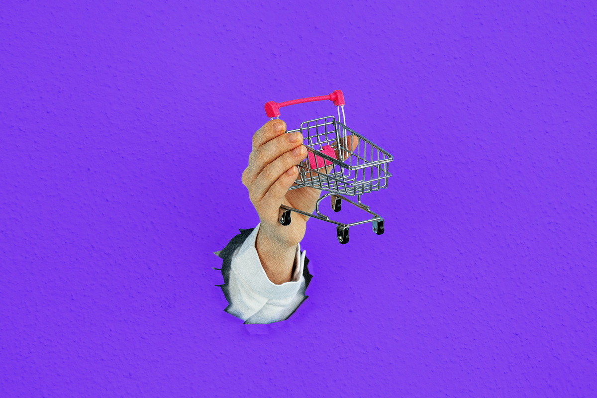 Image of a hand holding a tiny shopping cart aloft, coming out of a solid purple background.