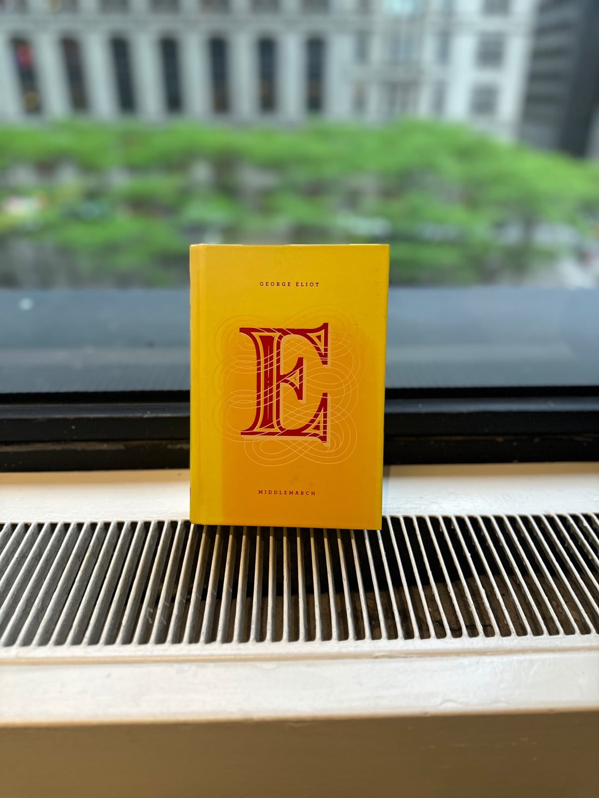 A copy of the book Middlemarch with some trees in the background out a window.