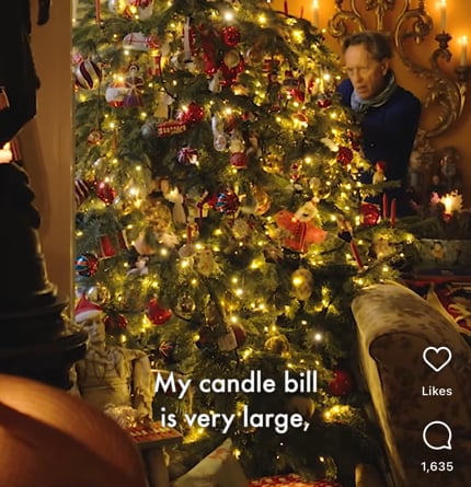 The actor Richard E. grant decorates a Christmas tree. The subtitle says, “My candle bill is very large.”