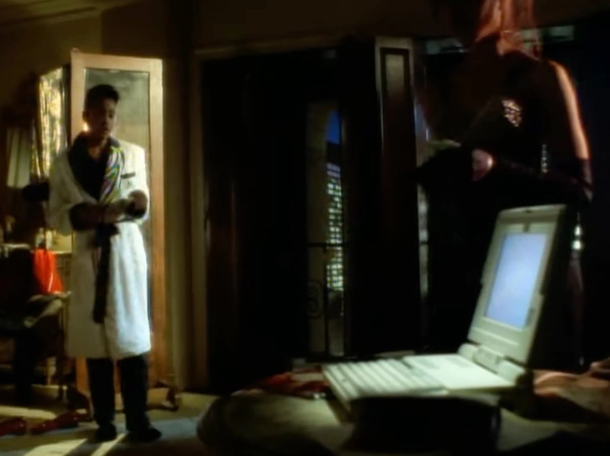 A screenshot from the song Jerk Out (1990) by The Time. A night scene in a dark room with skyscrapers out the window. Morris Day has told a beautiful woman he wants to sleep alone and asked her to leave her number by his “data bank,” which appears to be in the Compaq Presario line, and is the best-lit thing in the room. She is unhappy with this situation and about to leave. The eye cannot look away from the laptop. It is a sad situation but the laptop looks wonderful.