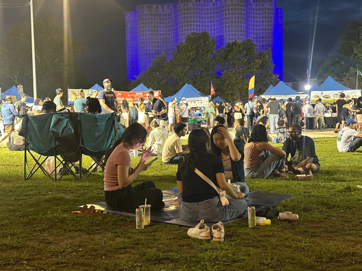 People in the grass at night with food stalls behind